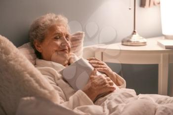 Senior woman with book sleeping in bed at night�
