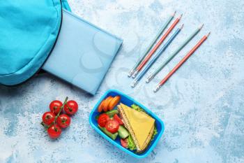 Lunch box with tasty food and school stationery on color background�