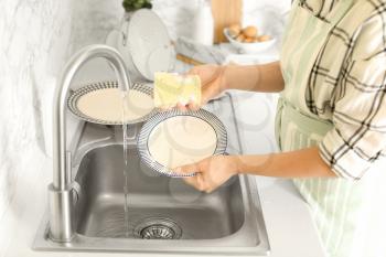 Woman washing dishes in kitchen sink�