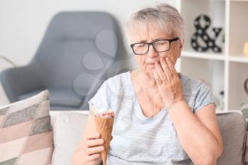 Senior woman with sensitive teeth and cold ice-cream at home�