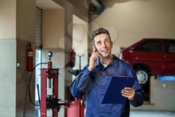 Male mechanic talking by phone in car service center�