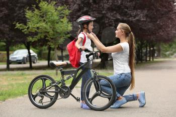 Mother helping her daughter to put on bicycle helmet outdoors�