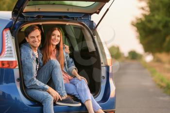 Happy couple sitting in trunk of their new car in countryside�