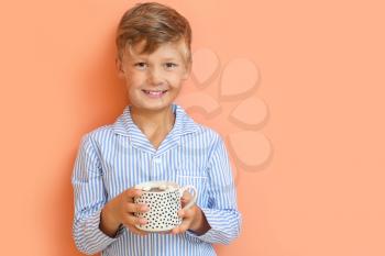 Cute little boy drinking hot chocolate on color background�