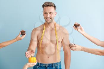 Handsome muscular man with measuring tape and hands suggesting him different food against color background. Weight loss concept�