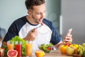 Handsome man counting calories while eating salad in kitchen. Weight loss concept�