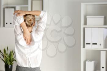 Young businesswoman practicing yoga in office, back view�