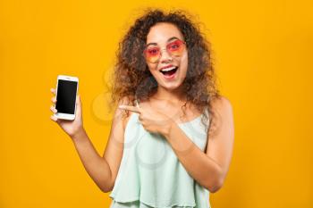 Portrait of happy African-American woman with mobile phone on color background�