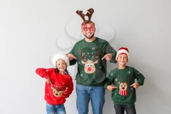 Funny man and his children in Christmas sweaters on light background�