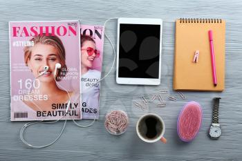 Modern tablet computer with fashion magazine, cup of coffee and female accessories on wooden background�