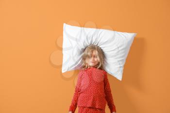 Sleepy little girl in pajamas and with pillow on color background�