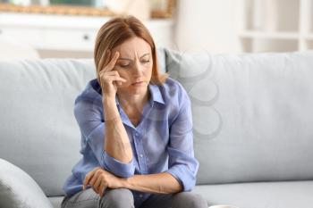 Stressed woman sitting on sofa at home�