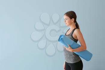 Young woman with yoga mat on color background�