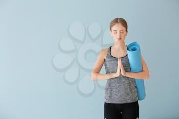 Young woman with yoga mat on color background�