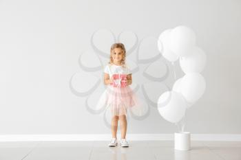 Little girl with balloons and gift near light wall�