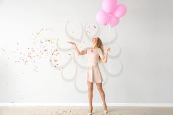 Beautiful young woman with balloons and confetti near light wall�