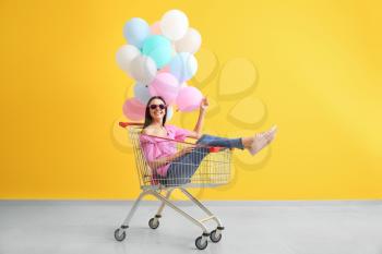 Young woman with shopping cart and balloons near color wall�