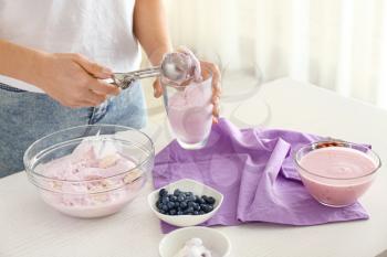 Woman putting tasty blueberry ice cream into glass in kitchen�