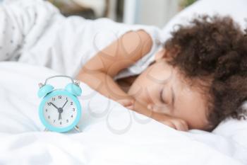 Little African-American girl with alarm clock sleeping in bed�