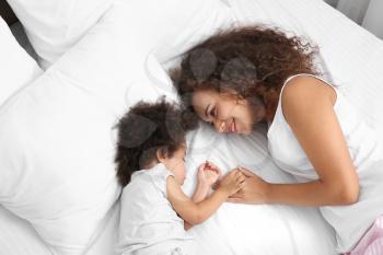 African-American mother with sleeping daughter lying on bed�