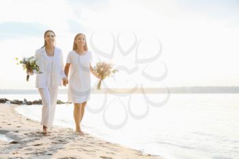 Beautiful lesbian couple walking along a river bank on their wedding day�