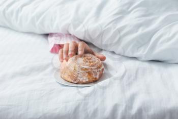 Young woman reaching hand for tasty bun while lying in bed�