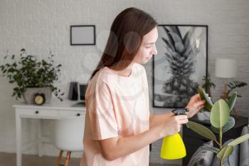 Young woman spraying water on houseplant at home�