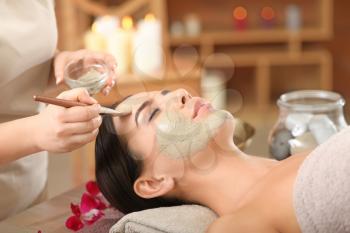 Cosmetologist applying mask onto face of young woman in spa salon�