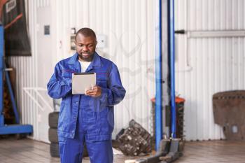 African-American mechanic with tablet computer in car service center�