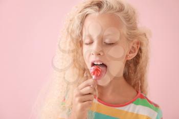 Cute little girl with lollipop on color background�