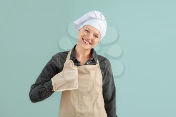 Beautiful female chef showing thumb-up on color background�