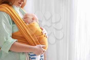 Young mother with little baby in sling at home�