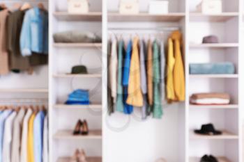 Big wardrobe with clothes in dressing room, blurred view�