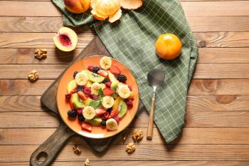 Plate with tasty fruit salad on wooden table�