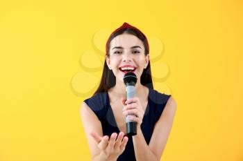 Beautiful young female singer with microphone on color background�