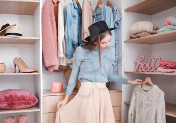 Beautiful young woman choosing clothes from large wardrobe�