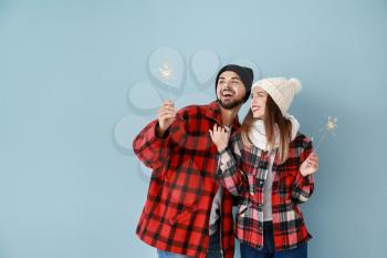 Happy young couple with Christmas sparklers on color background�