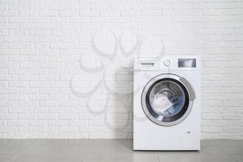 Modern washing machine with laundry near white brick wall�