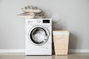 Modern washing machine with laundry near white wall�