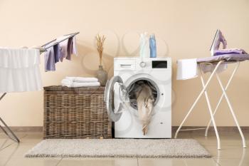 Modern washing machine with laundry, clothes dryer and ironing board near color wall�