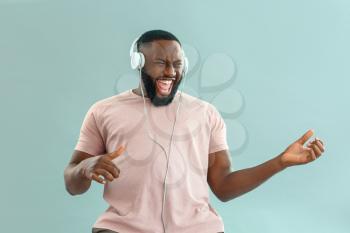 Emotional African-American man listening to music on color background�