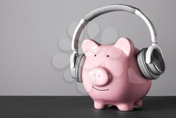 Piggy bank with headphones on grey background�