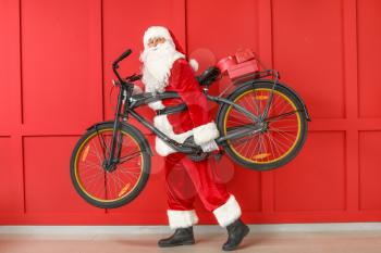 Santa Claus with Christmas gifts and bicycle on color background�