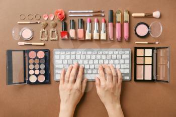 Hands of female beauty blogger with PC keyboard and set of decorative cosmetics on color background�