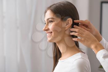 Woman putting hearing aid in young girl's ear at home�