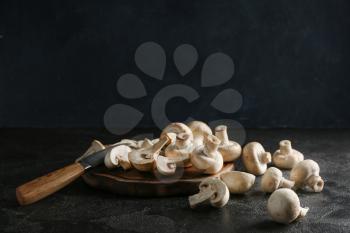 Cutting board with fresh mushrooms and knife on dark background�