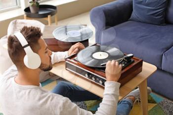 Young man listening to music through record player at home�