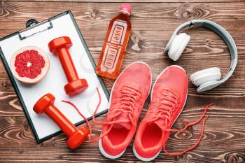 Dumbbells with clipboard, shoes, headphones and bottle of water on wooden background�