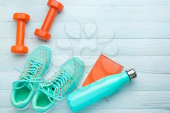 Dumbbells with notebook, shoes and bottle of water on white wooden background�