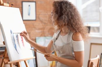 Beautiful female African-American artist painting in studio�